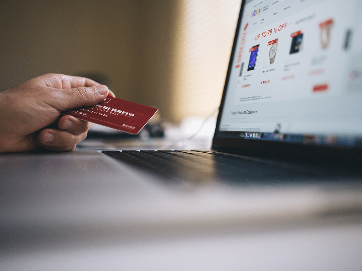 Persona con tarjeta de credito al lado de un portatil para pagar online.